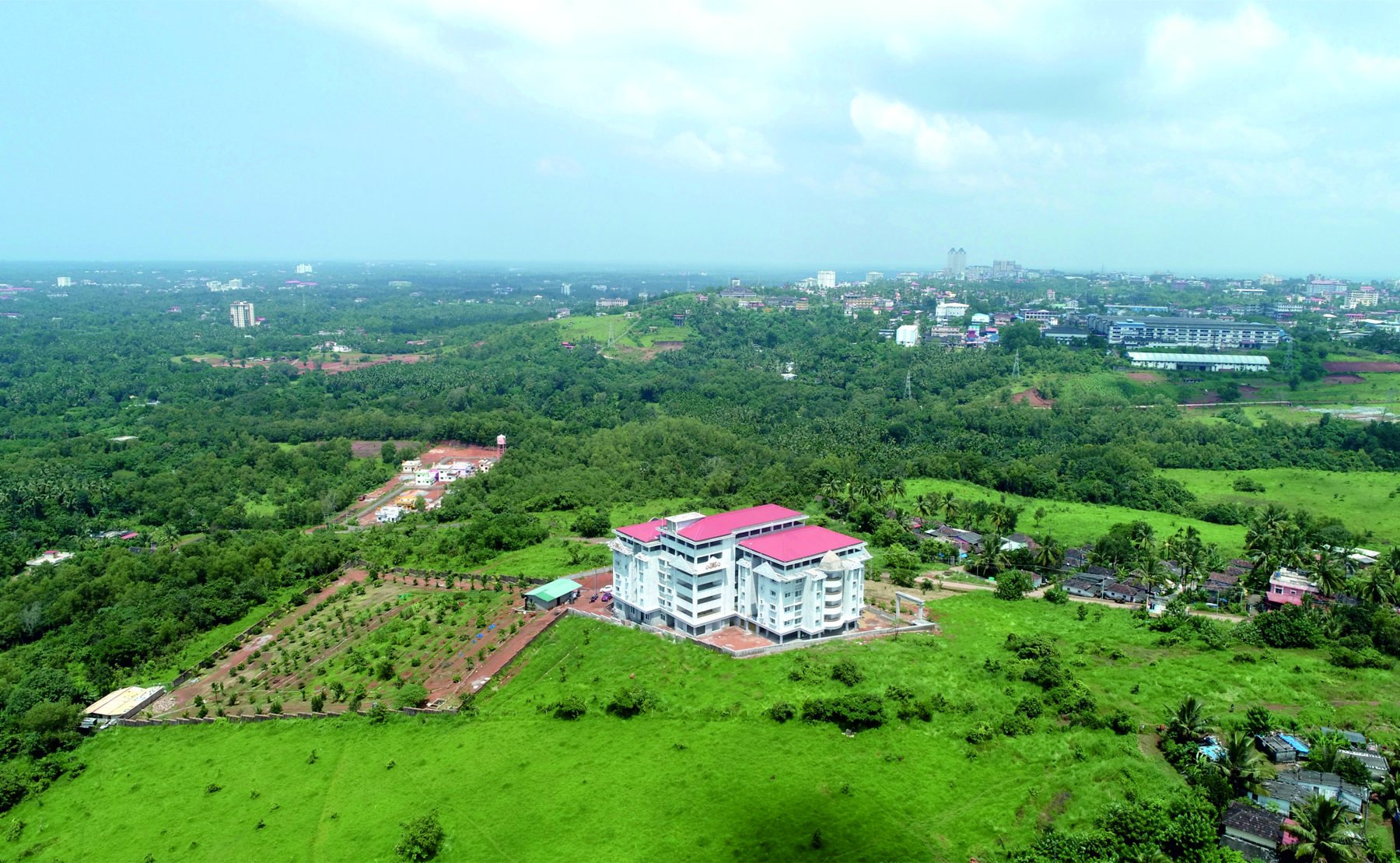 Aerial view of the Green Valley Paradise campus surrounded by green fields, with Manipal in the distance